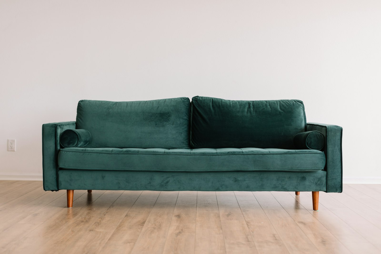 A green velvet three-seater sofa with wooden legs